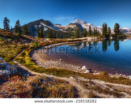 Curving mountain lake shore with perfect reflection, blue sky, and distant mountains