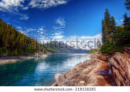 Bright blue mountain creek with a path along the shore and scenic trees and mountains