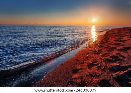 Warm ocean beach sunrise with breaking wave and footprints in sand