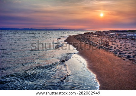 Crystal waters on sandy beach shore with distant cliffs and dusty pink and purple skies