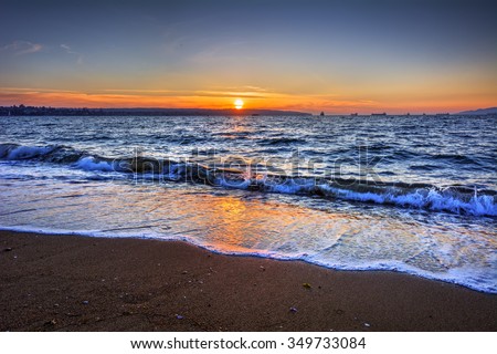 Waves breaking on the beach, orange sunset, and ships on the horizon
