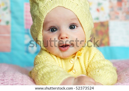 stock photo : Baby Girl in Yellow Knit Hooded Sweater in Front of Quilt
