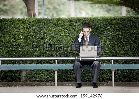 very busy businessman talking on phone and using laptop computer at the bus stop