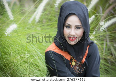 Beautiful Young Thai Muslim Woman with Abaya Dressed Outdoors. Enjoy Nature. Healthy Smiling Girl in Green Grass.