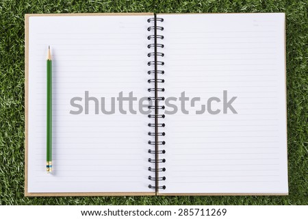notebook paper background with pencil on green grass background