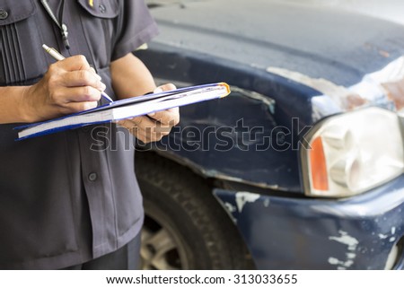 Side view of writing on paper while insurance agent examining car after accident