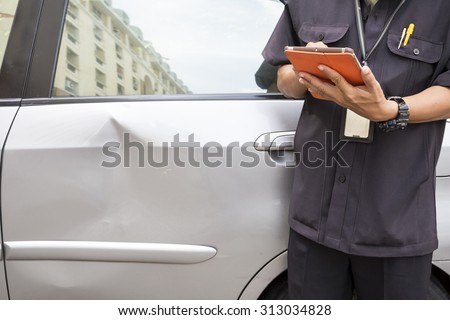 Side view of writing on tablet computer  while insurance agent examining car after accident