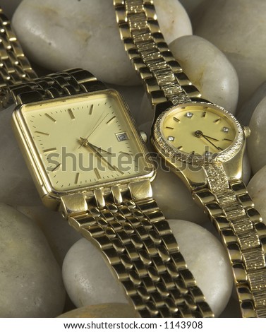 Gold ladies and mens watches on white pebble background