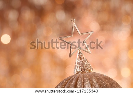 gold christmas baubles with star on top on background of defocused golden lights.