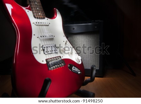 red and white electric guitar and combo amplifier on black background