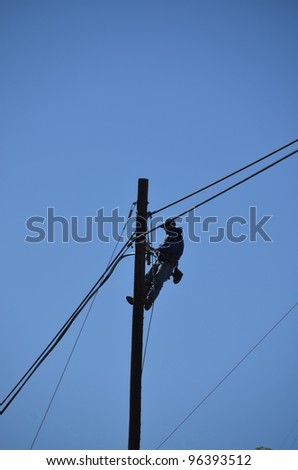 An electrician silhouetted against the blue sky at the top of a pole while performing maintenance on electric powerlines