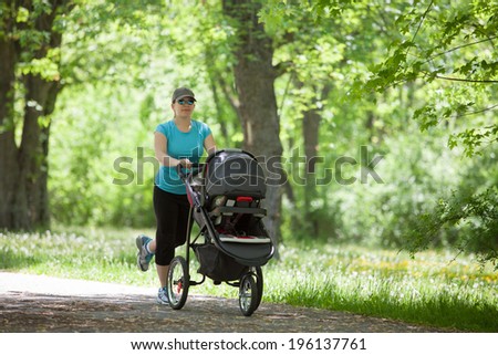 Young mother running while pushing a stroller in the park