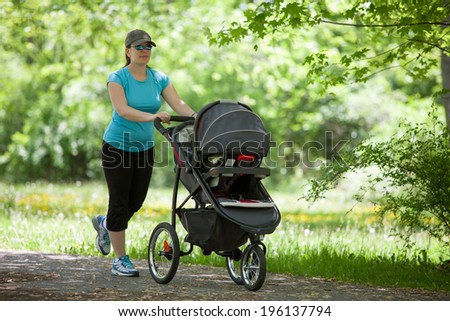 Young mother running while pushing a stroller in the park