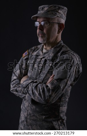 Military man standing with folding arms, studio low key