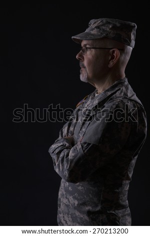 Military man standing with folding arms, studio low key