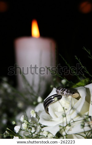 Wedding rings on a white rose with candle in background