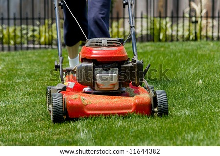 Person walking behind a red lawn mower on green grass.