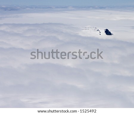 Aerial of a snow covered mountain top, poking through cloud. Text space.