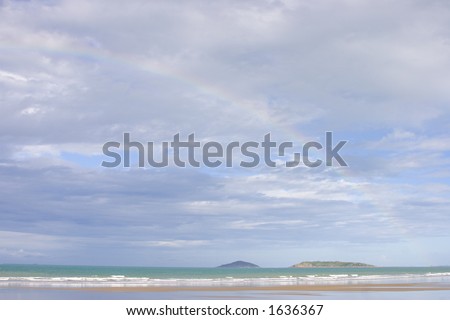A rainbow on a beach in the Whitsunday Islands, Australia. In the background are Round-top and Flat-top islands.