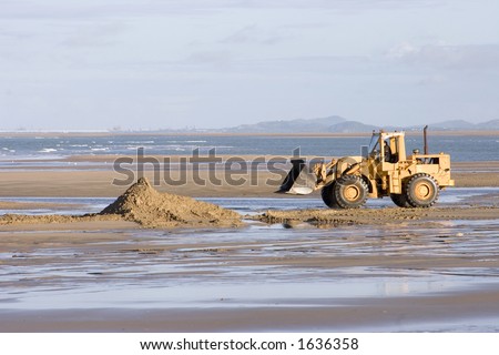 A large yellow digger moving sand on an Australian beach.