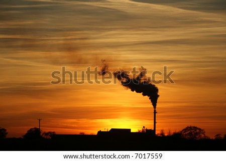 A beautiful sunset and dramatic sky behind a factory with a smoking chimney