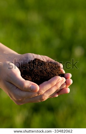 Hands holding soil against a green background. Shallow depth of field. Focus is on the soil