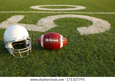 American Football and Helmet on the Field with the Fifty Yard Line in the Background