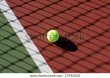 Tennis ball on the court in the shadow of the net