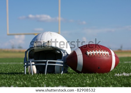 American Football and Helmet on the Field with Goal Posts in the background