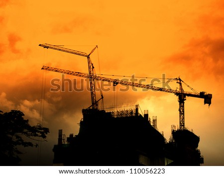 Crane on tower in construction site silhouette with sunset sky