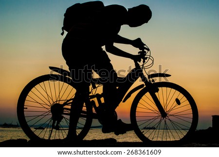 Silhouette of backpacker ride mountain bike on bridge beside sea with sunset sky background