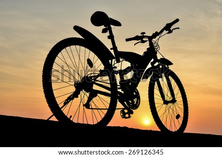 Silhouette of mountain bike parking on jetty beside sea with sunset sky background