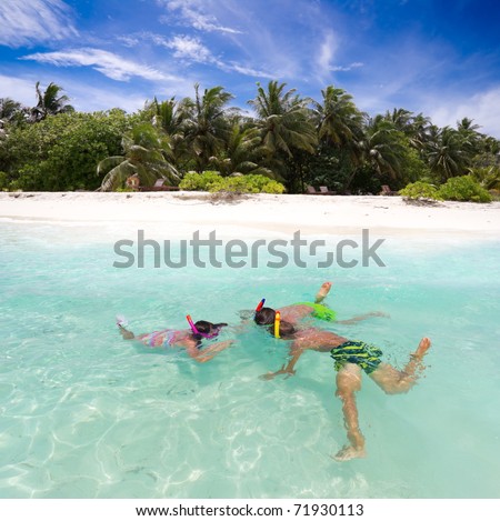 Three smiling siblings, one girl and two boys, swimming while wearing snorkeling gear in the ocean of the Maldives.
