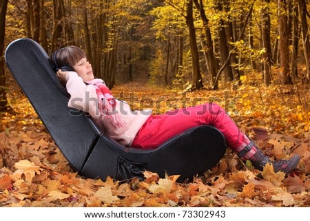 Girl sitting in an ergonomic chair listening to music outside in the autumn leaves.