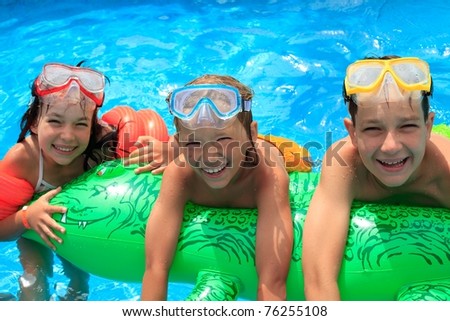 Closeup of smiling young brothers and sister in swimming pool with inflatable toy.