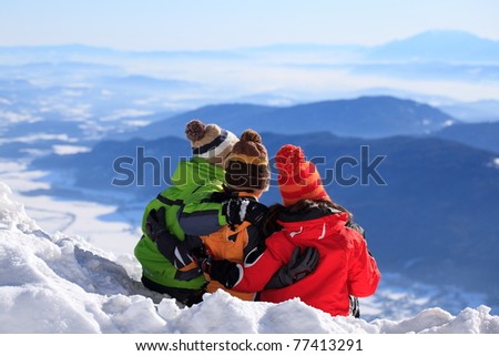 Two happy brothers and sister in woolly hat on snow mountainside in Winter.