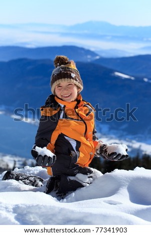 Portrait of happy young boy playing with snow on Alpine mountain summit.