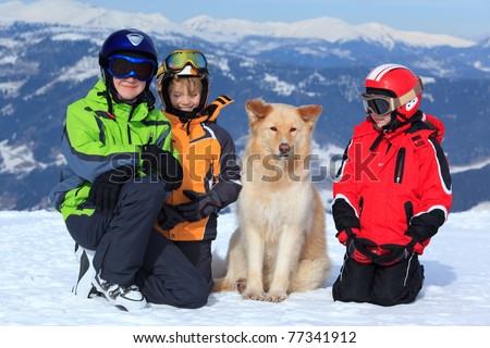 Three children in ski clothing on snowy Alpine mountain with pet dog.