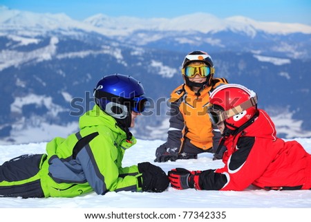 Two happy brothers with sister in ski helmets and goggles on snowy Alpine mountain.