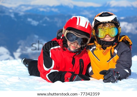 Smiling young boy and girl in ski helmets and goggles on snowy Alpine mountain summit, Winter scene.