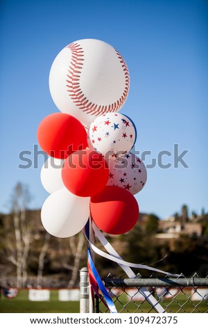 Cluster of balloons with a baseball balloon tied to a chain link fence at a baseball field on opening day