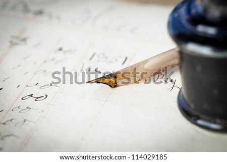 Close up of a quill pen laying on a page of an old ledger next to an antique ink bottle