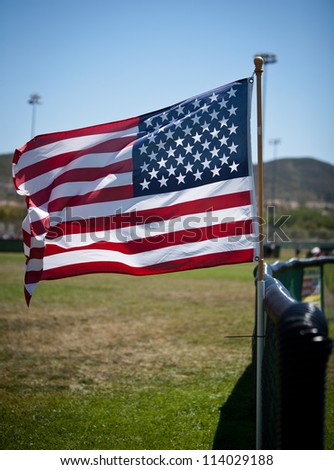 Vertical color shot of an American flag mounted to the fence of a ball field