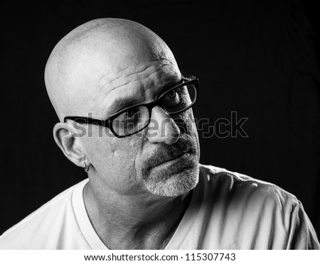 black and white head shot of a middle aged stern looking bald man with facial hair looking off to camera left on a black background