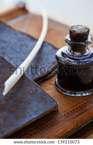 Antique quill pen and glass ink bottle with cork stopper on top of an antique leather bound ledger along with two leather antique small folders