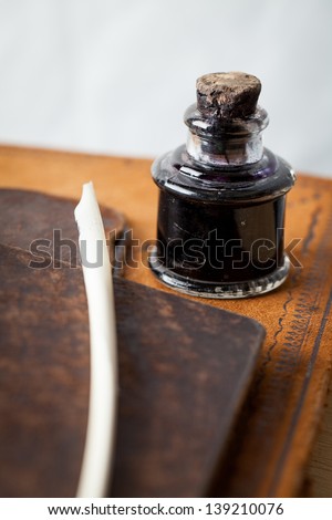 Antique quill pen and glass ink bottle with cork stopper on top of an antique leather bound ledger along with two leather antique small folders