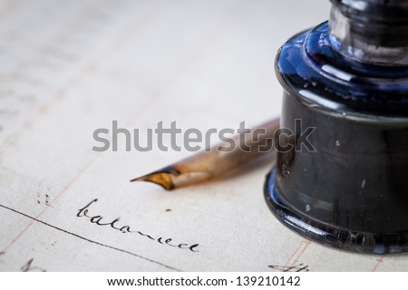 Close up of a page out of an antique accounting ledger with an old feather quill pen and an antique glass inkwell