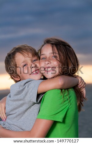 Close up shot of a brother and sister hugging each other with a beautiful sunset in the background