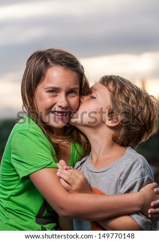 Close up shot of a sister hugging her brother and him kissing her on the cheek with a beautiful sunset in the background