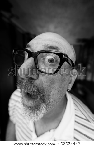 Isolated shot of a bald older man with a goatee looking into a wide angle lens looking surprised wearing black frame eyeglasses